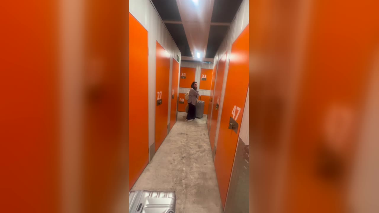 Karol Barbosa com uma mala no fim do corredor de portas laranja do depósito em Madri onde as malas foram furtadas